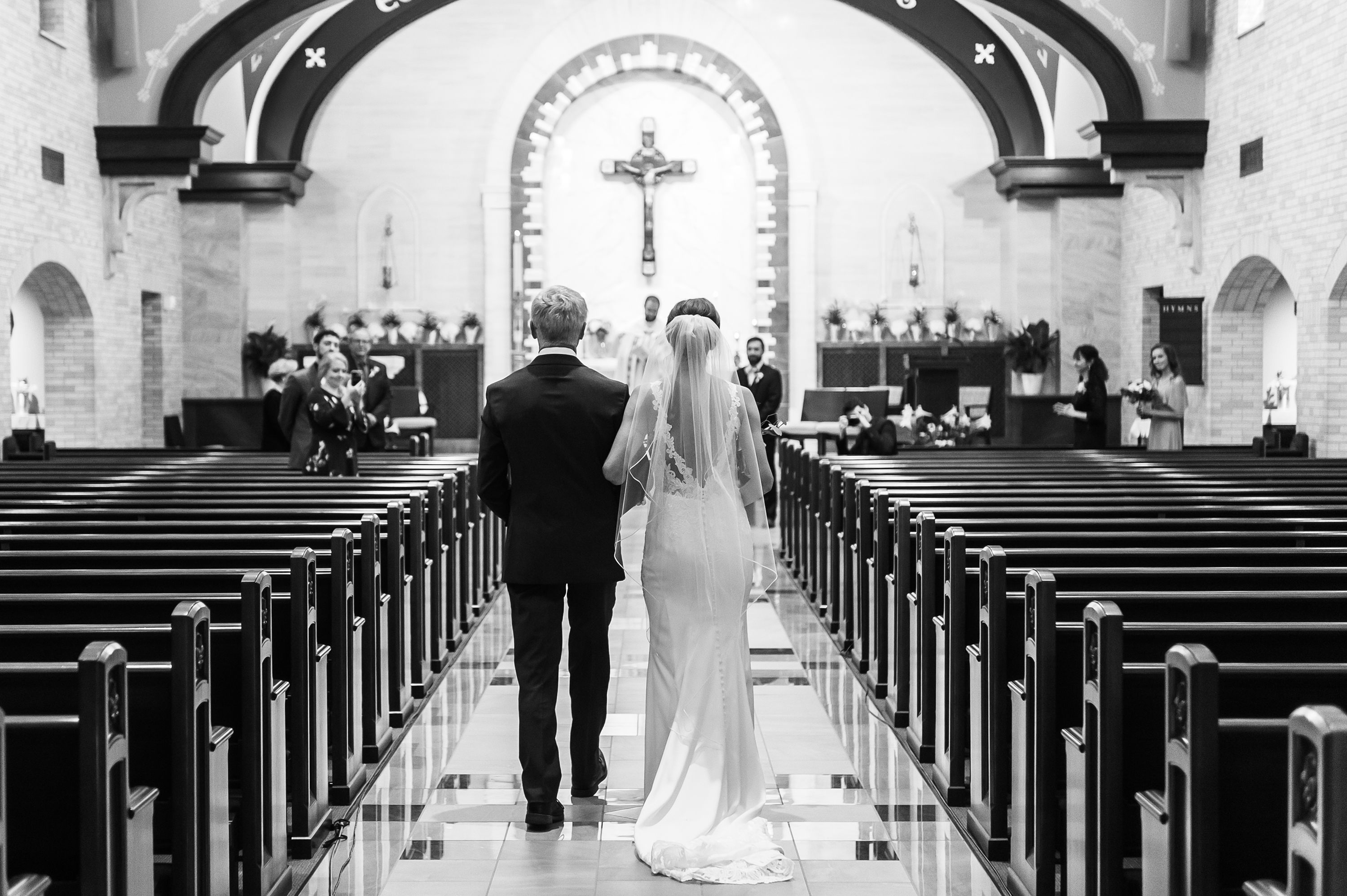 The bride walks in with her father to an empty church at Our Lady of Lourdes Catholic Church in Denver, Colorado.