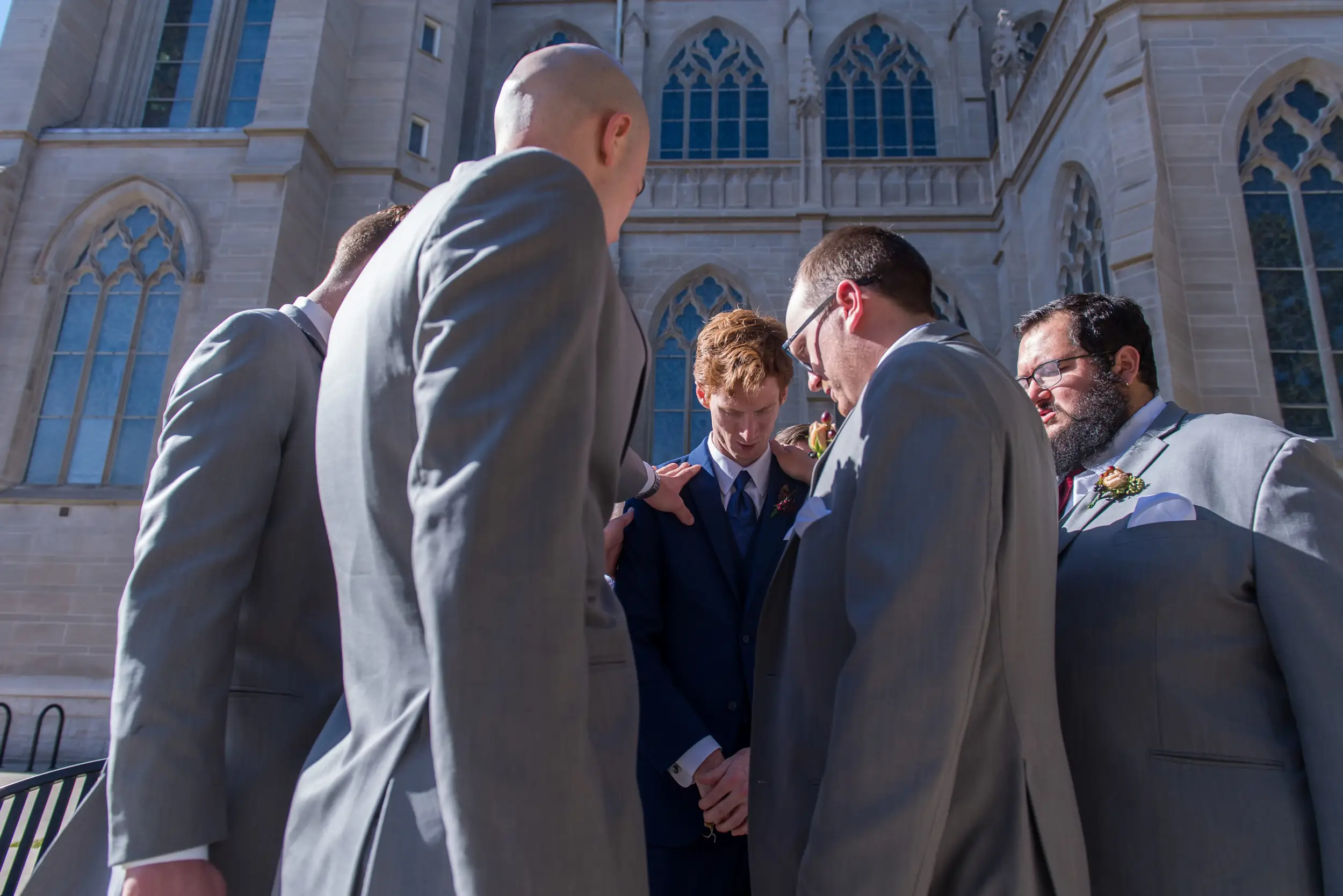 Groomsmen pray over the groom before his Cathedral Basilica of the Immaculate Conception wedding in Denver, Colorado.