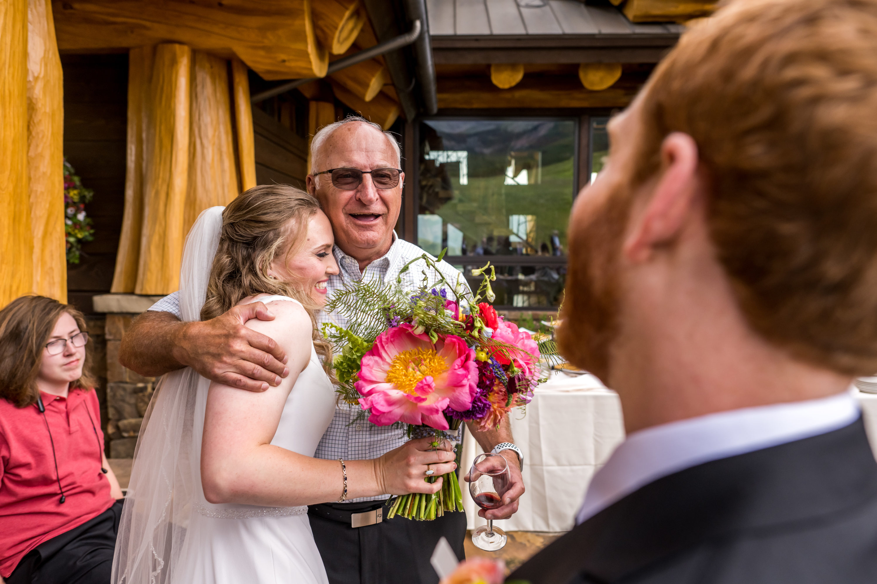 The bride embraces a family member as the groom looks on during their wedding in Telluride, Colorado.