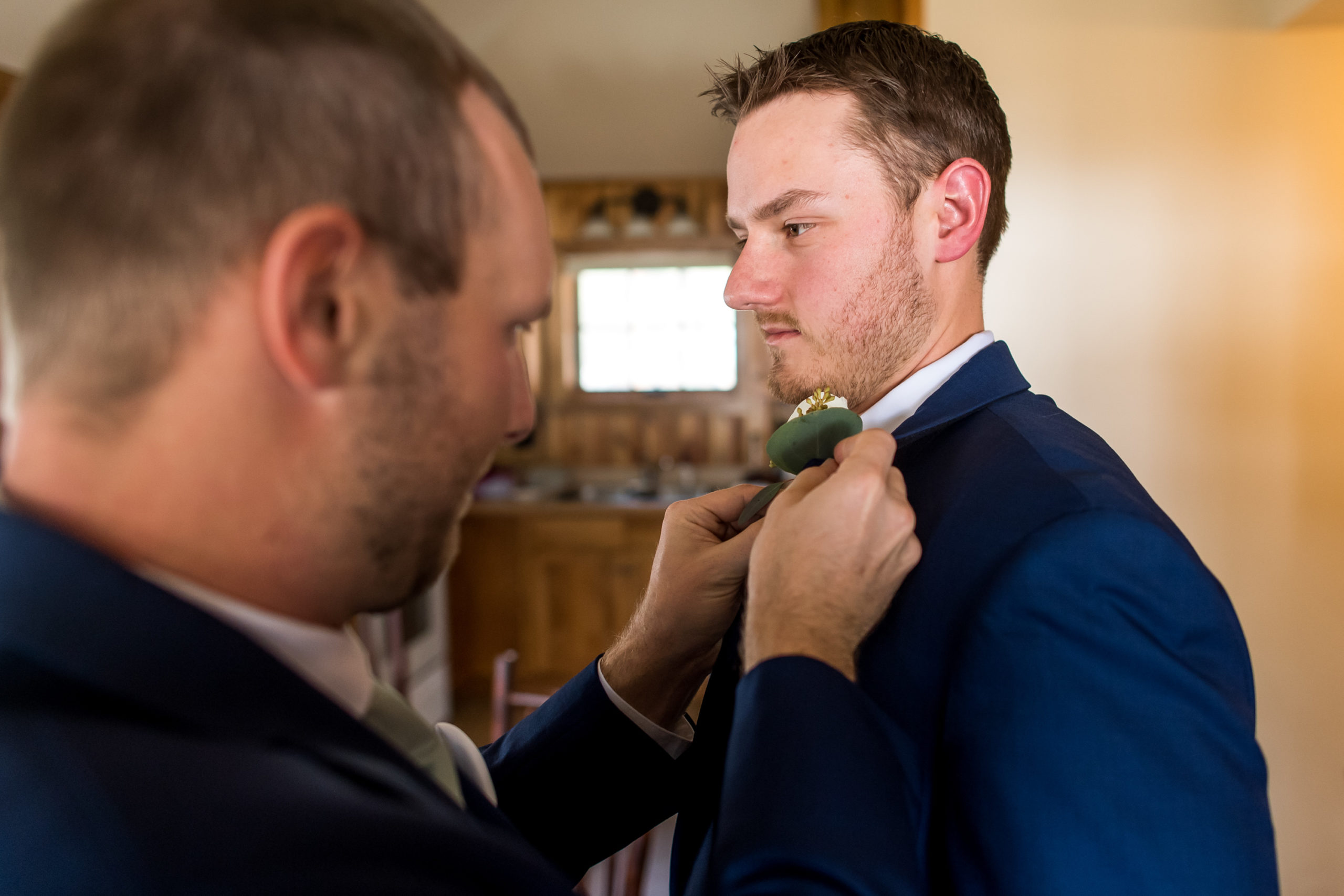 A groomsman pins on the groom's boutonniere during his YMCA of the Rockies wedding in Estes Park, Colorado.