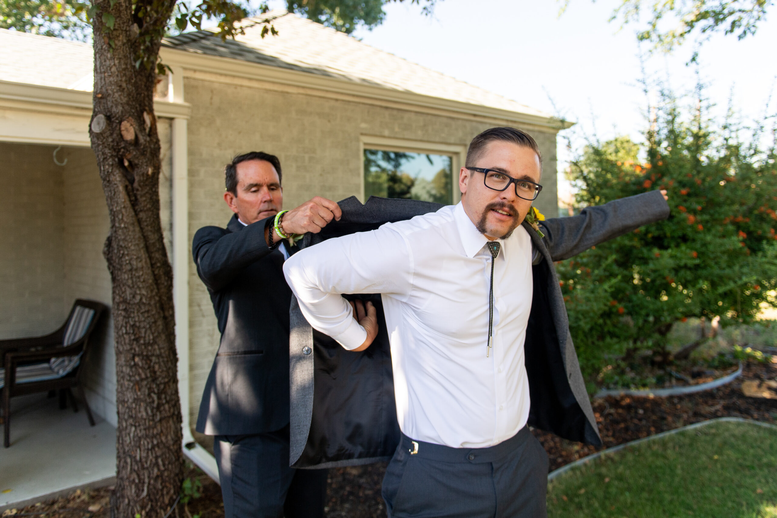 A father puts on a jacket on a groom before a Holy Ghost Church Denver wedding in Denver, Colorado.