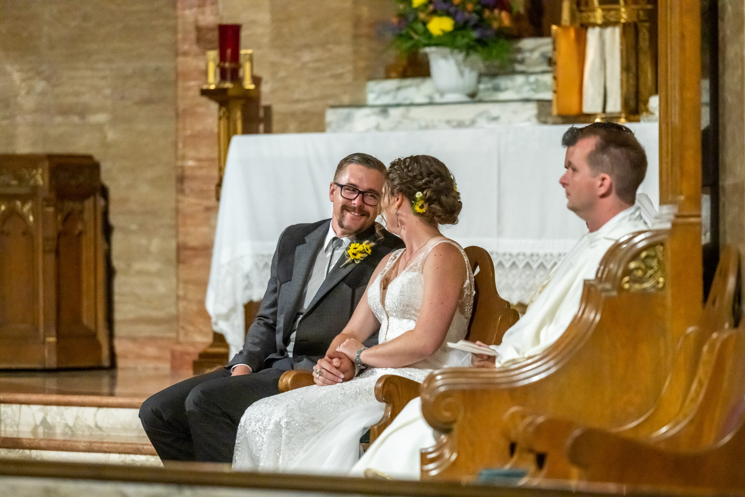 A groom smiles at his bride during their Holy Ghost Catholic Church wedding in Denver, Colorado, while seated near the altar.