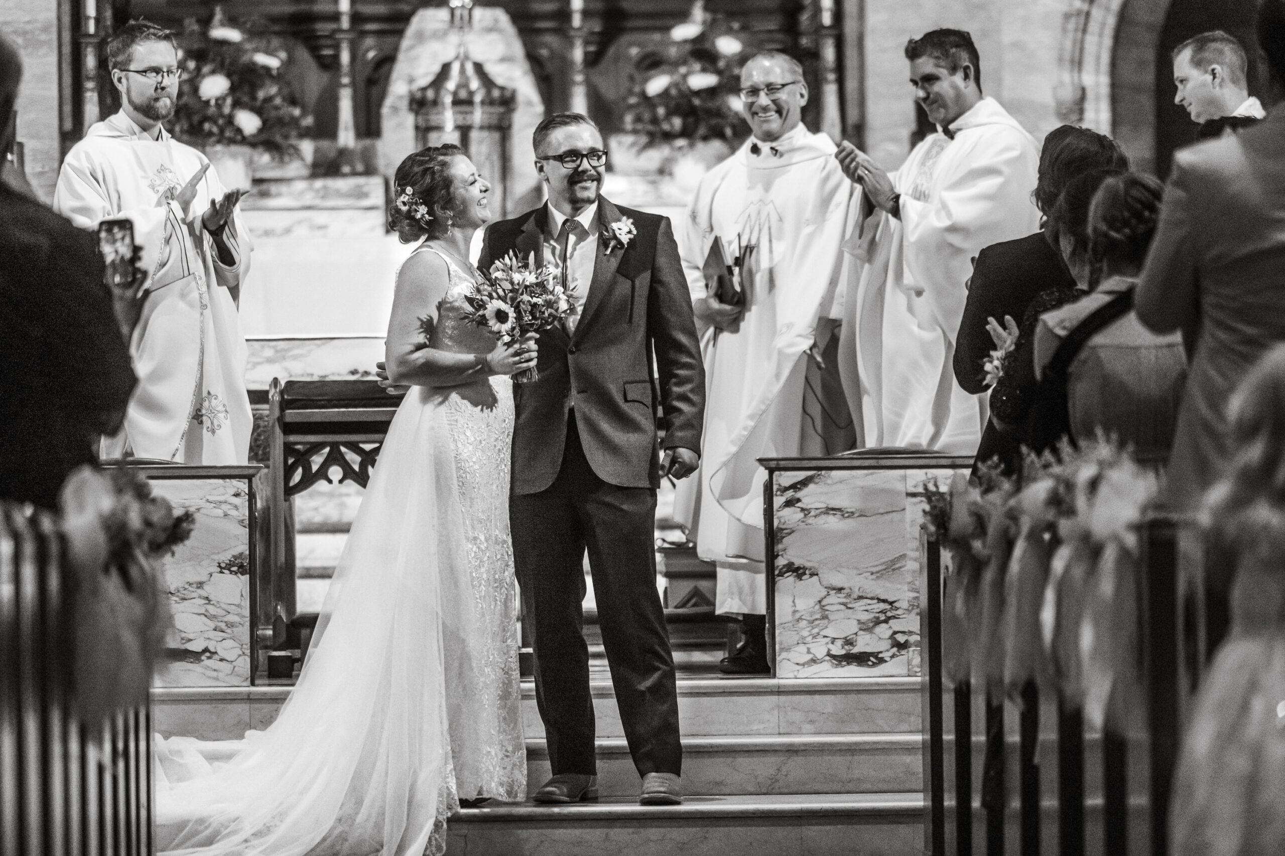 A bride and groom smile before attendees at their wedding at Holy Ghost Catholic Church in Denver, Colorado.