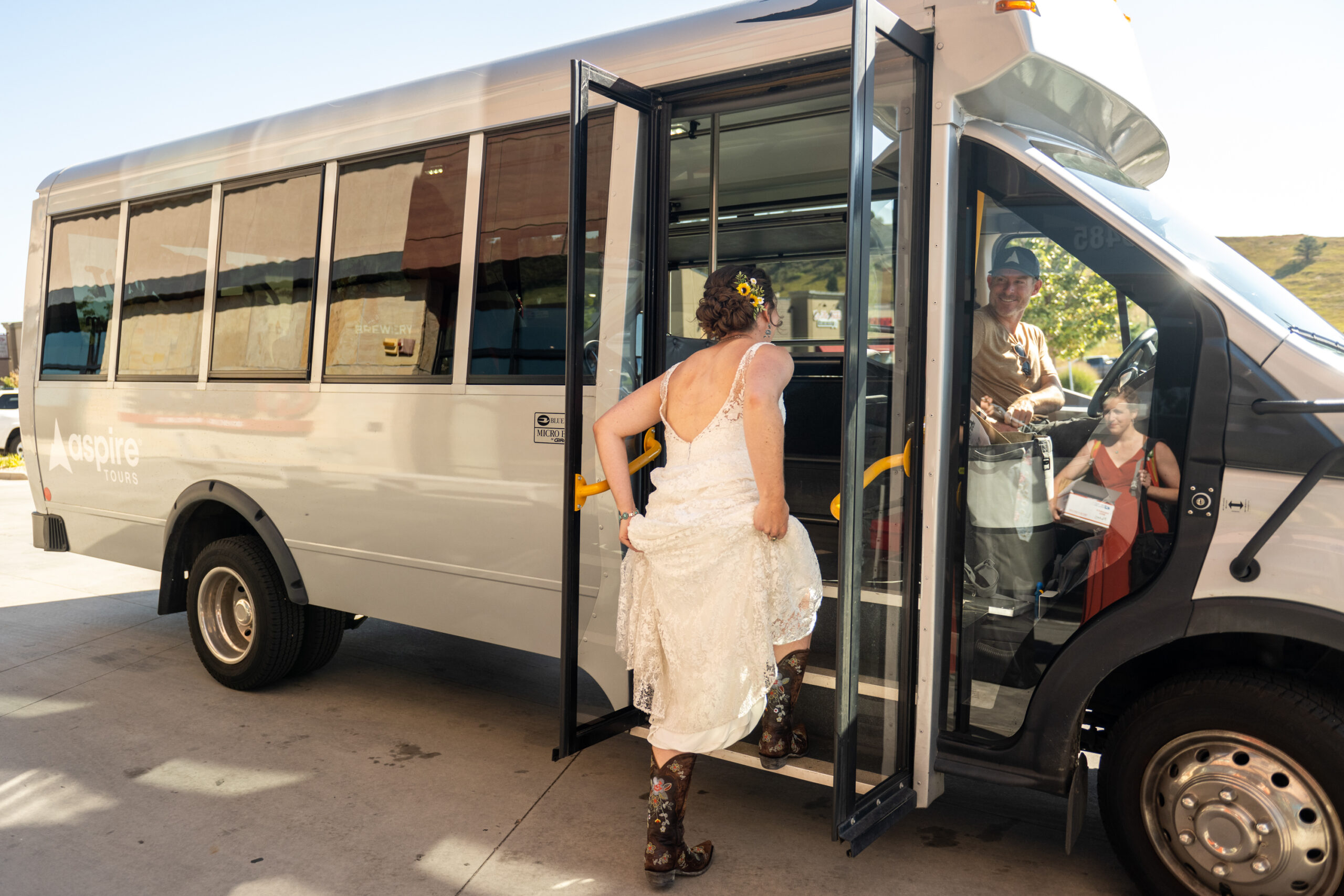 A bride boards a bus wearing cowgirl boots before a Holy Ghost Church Denver wedding in Denver, Colorado.