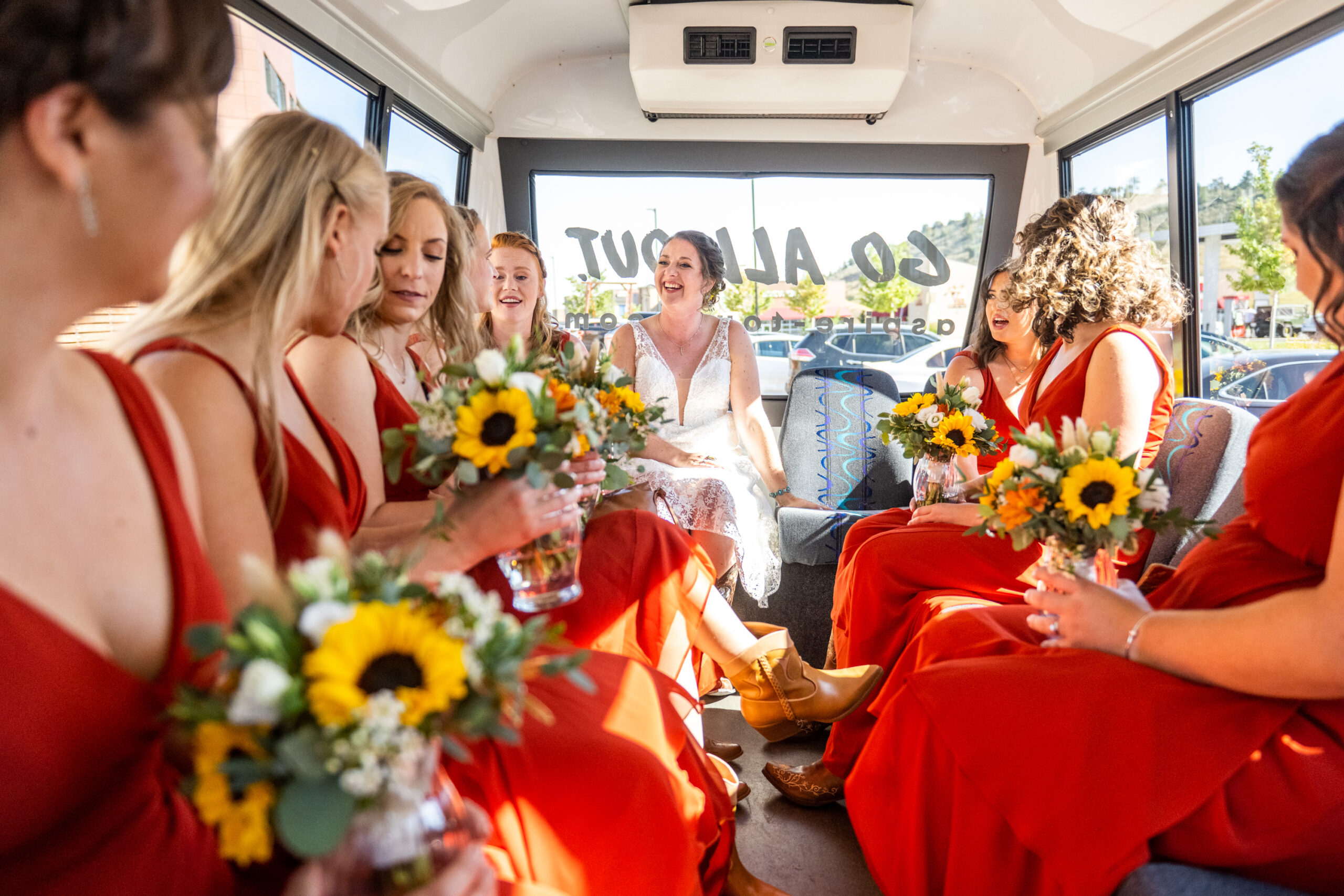 A bride and her bridesmaids sit around a bus on their way to a Holy Ghost Church Denver wedding in Denver, Colorado.