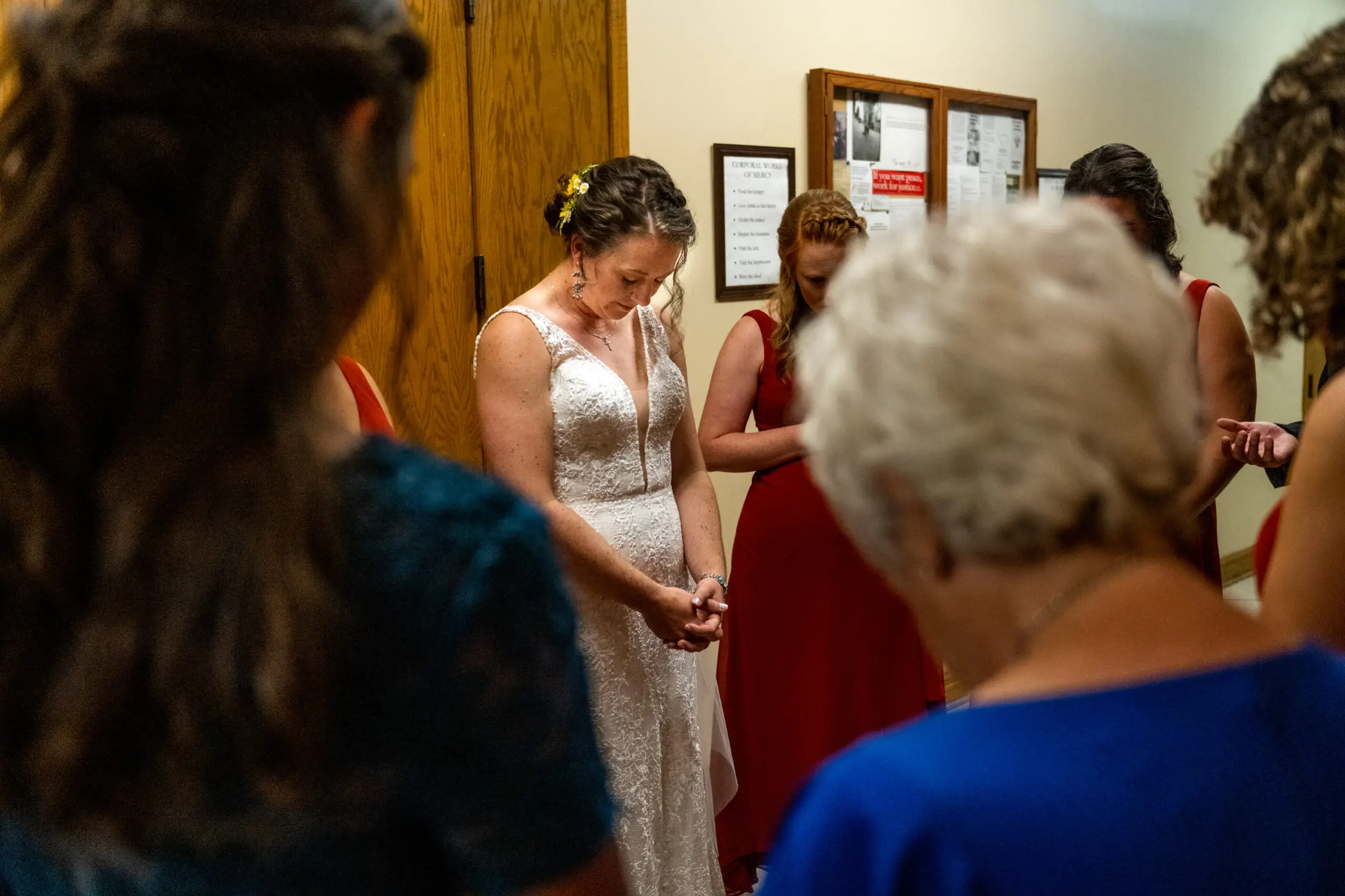 A bride prays in the basement of a church surrounded by her family and bridesmaids before a Holy Ghost Catholic Church wedding in Denver, Colorado.