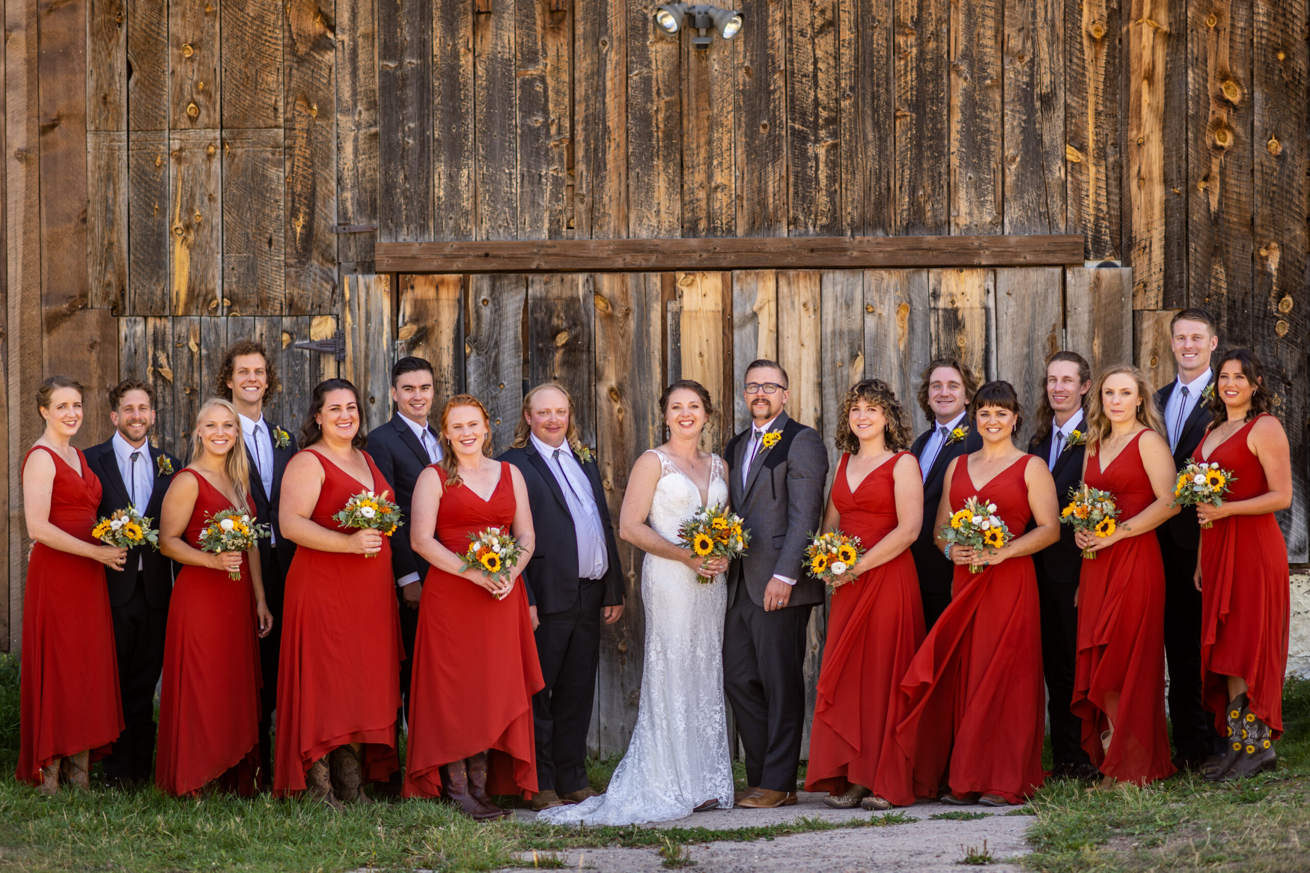 The bridal party pose for a photo in front of a barn at Three Sisters Park in Evergreen, Colorado.