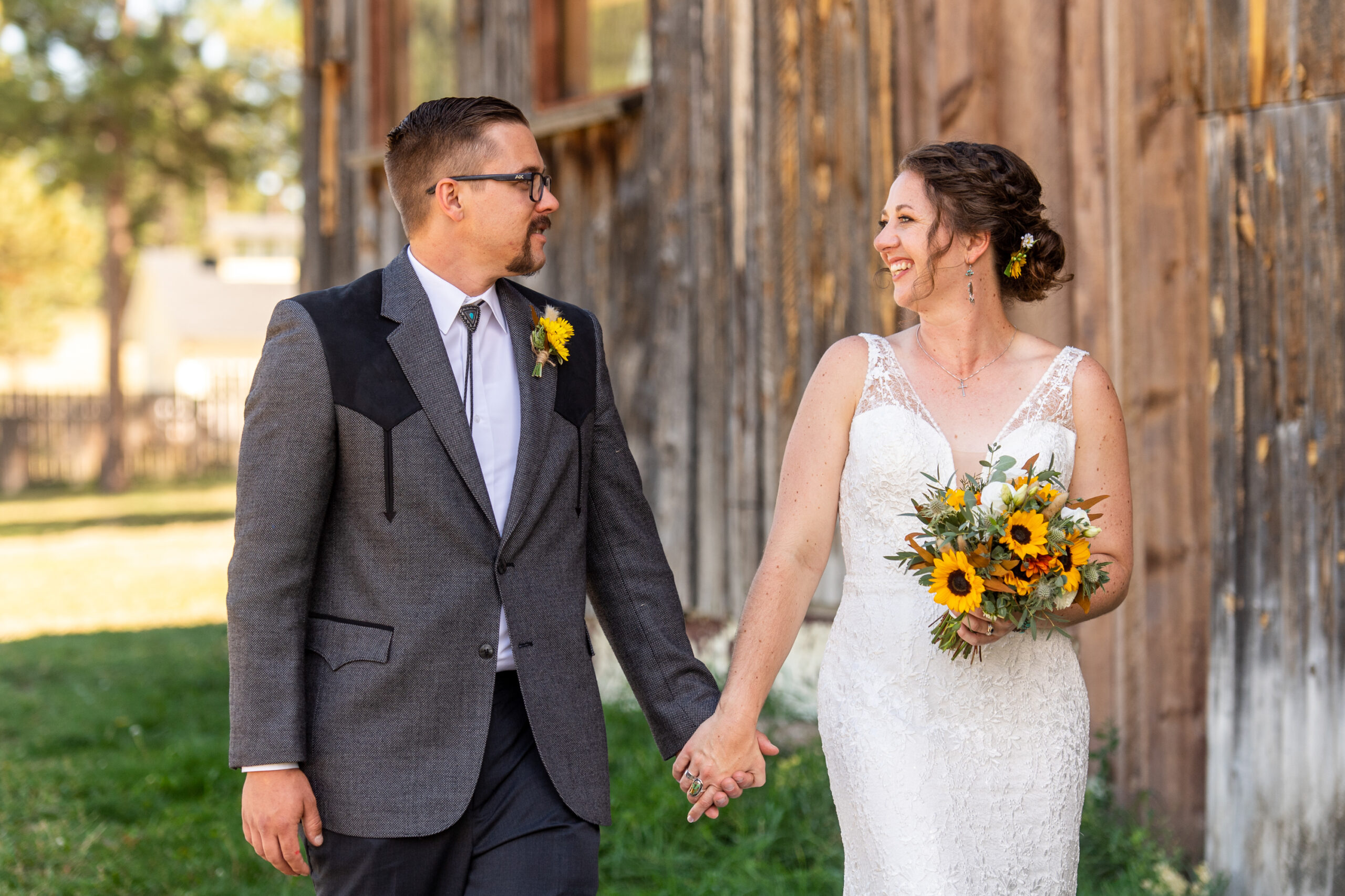 A groom and bride look at each other's eyes while holding hands next to a brown barn at Three Sisters Park in Evergreen, Colorado.