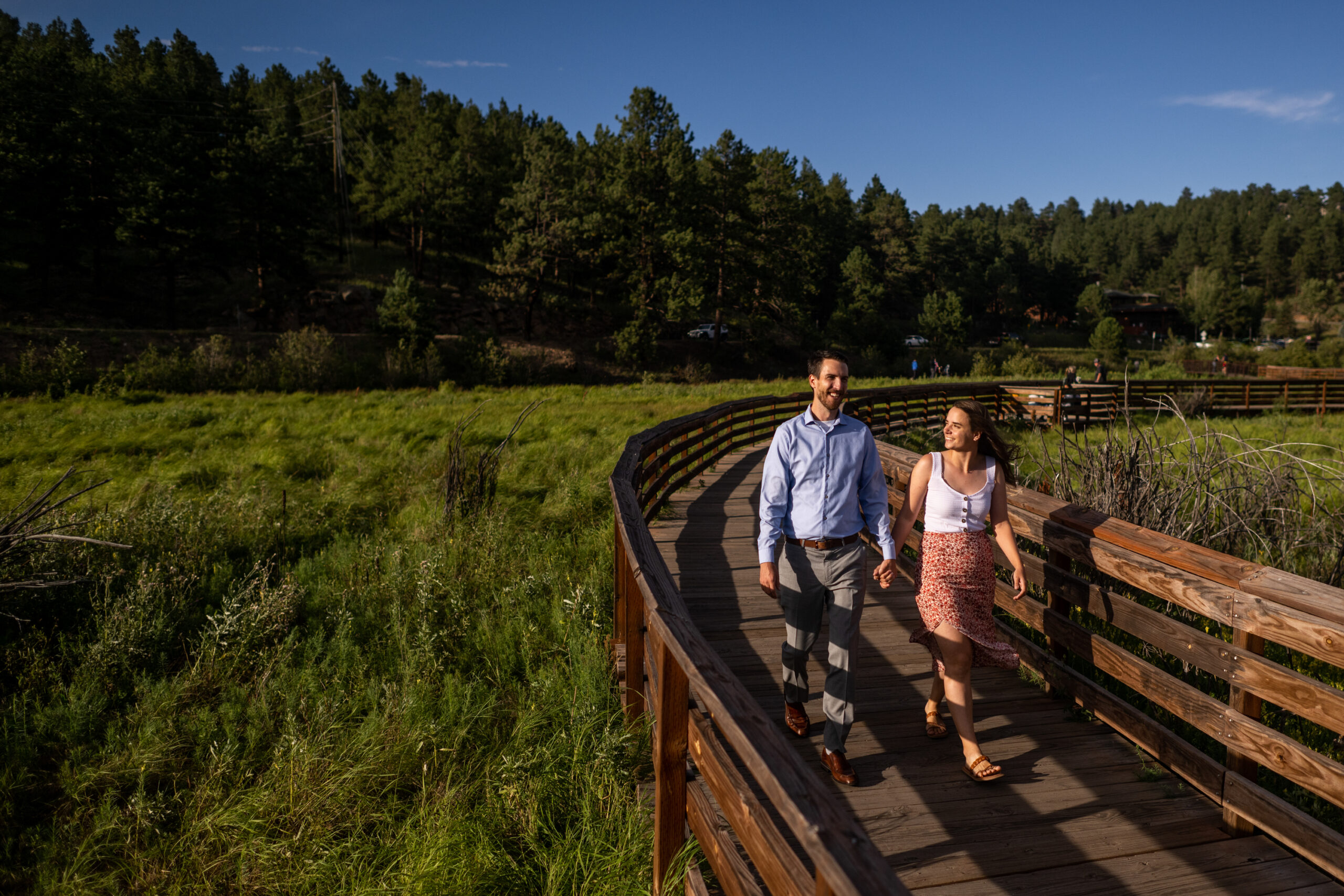 Alice and Joe walk along a boardwalk during an engagement photo shoot at Evergreen Lake in Evergreen, Colorado.