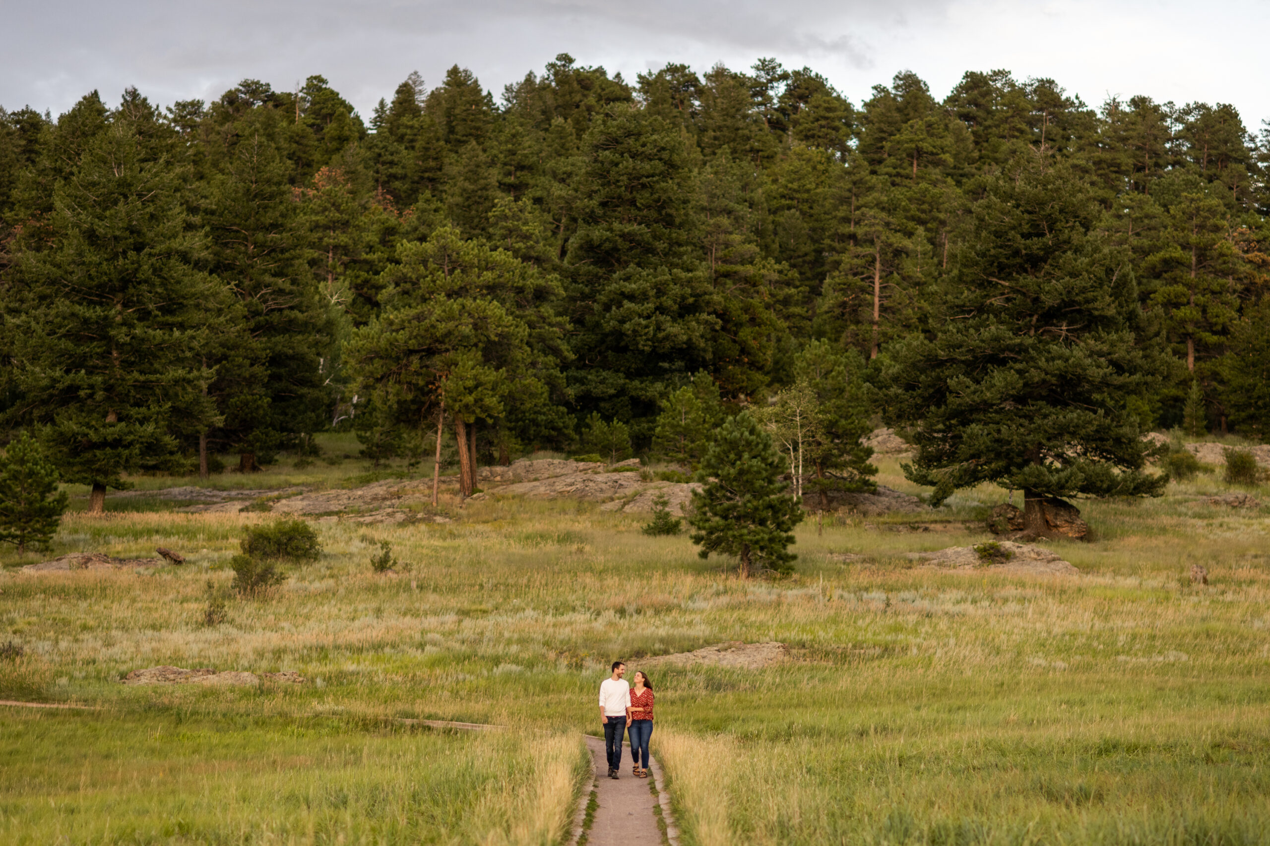 Alice and Joe walk holding hands during an engagement photo shoot at Three Sisters Park in Evergreen, Colorado.