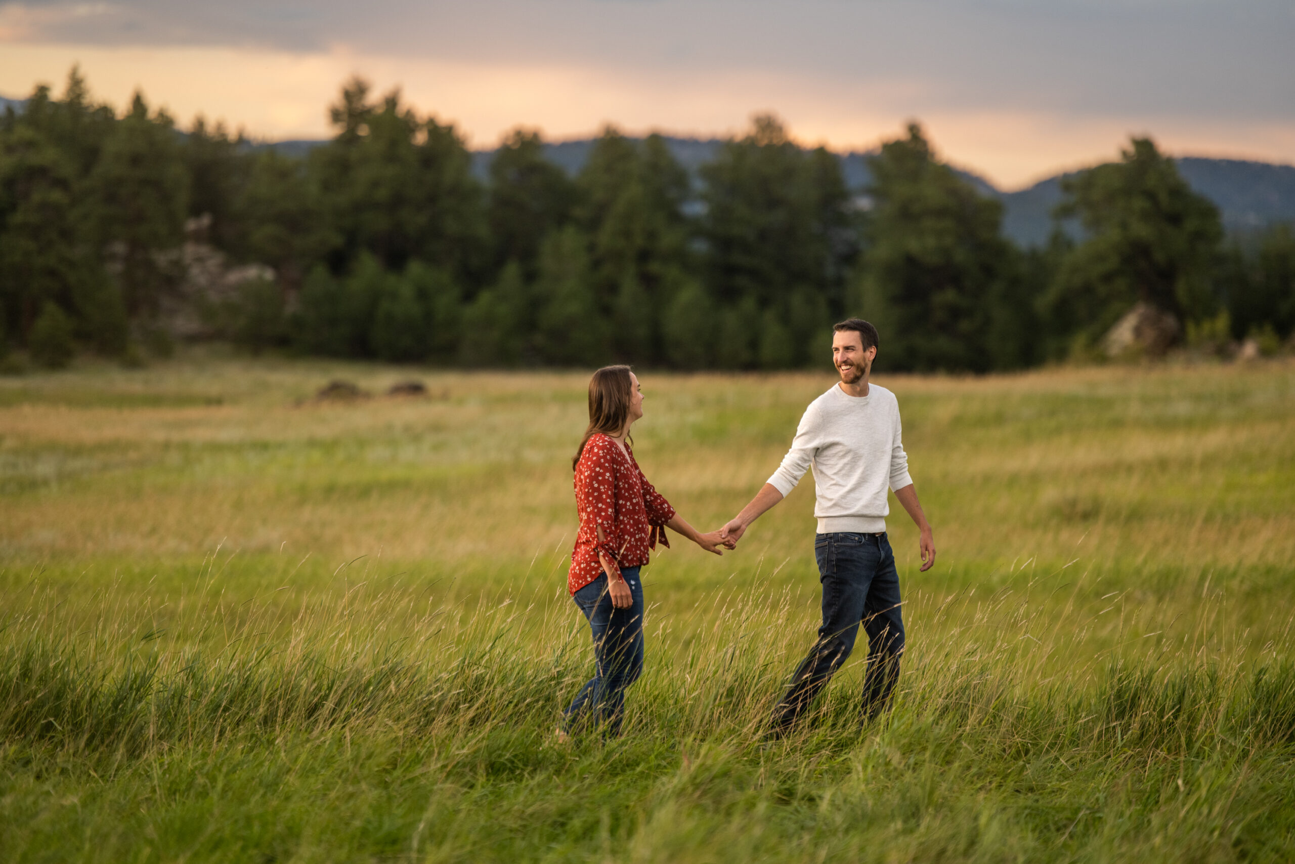 Alice and Joe walk holding hands during an engagement photo shoot at Three Sisters Park in Evergreen, Colorado.