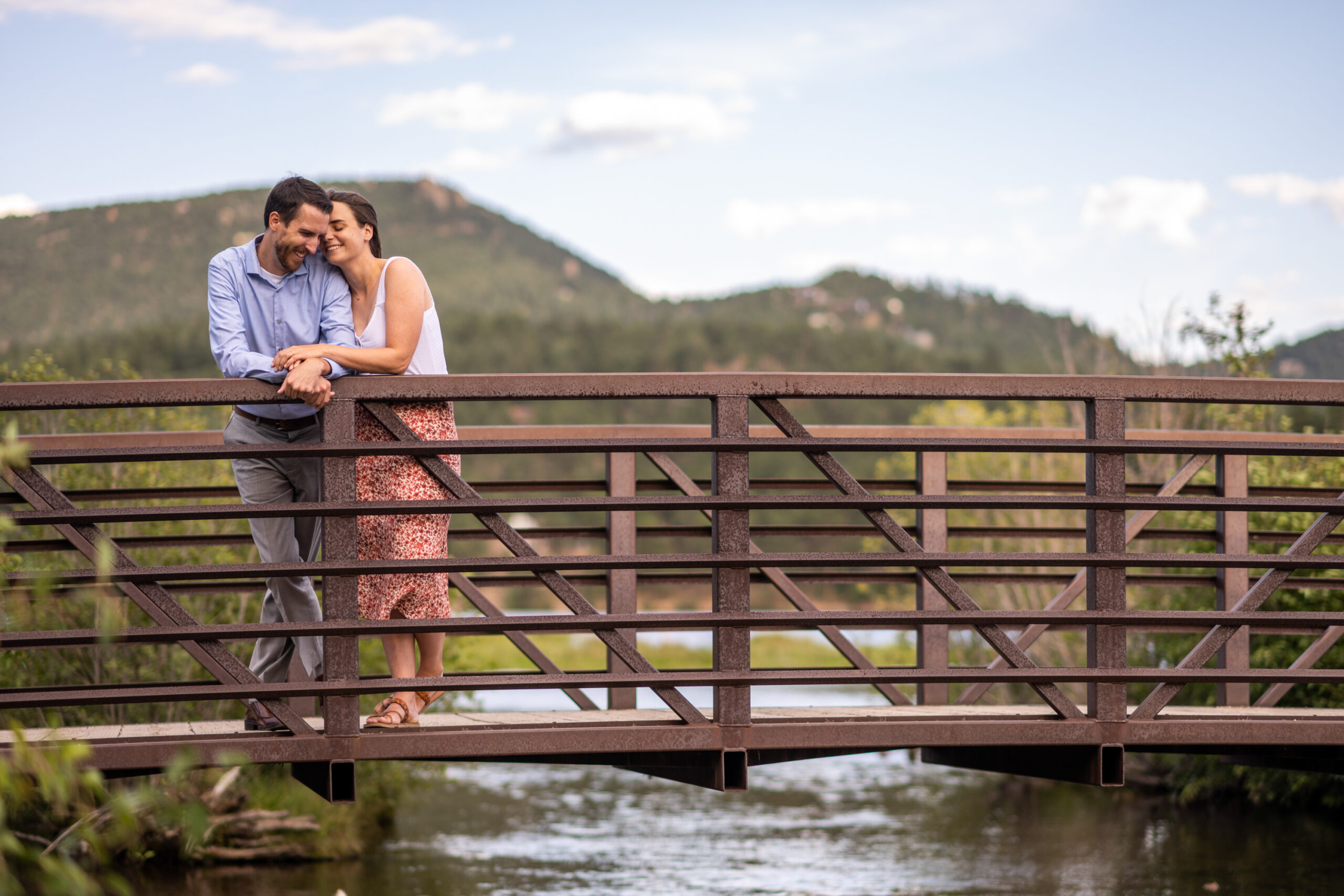Alice and Joe hug on a bridge during an engagement photo shoot at Evergreen Lake in Evergreen, Colorado.