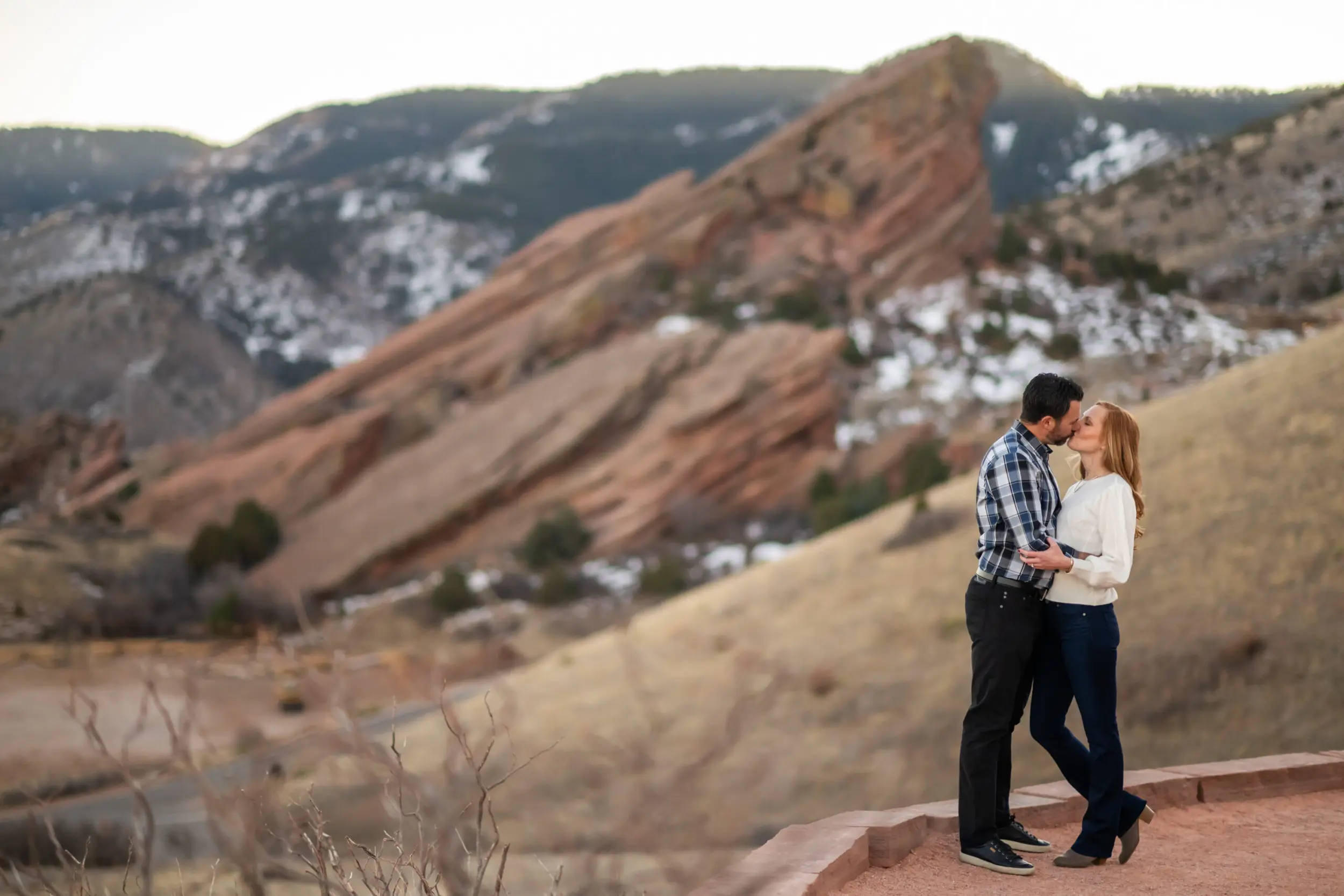 A couple kisses on the trail at Red Rocks Park and Amphitheatre during a Red Rocks engagement session in Morrison, Colorado.