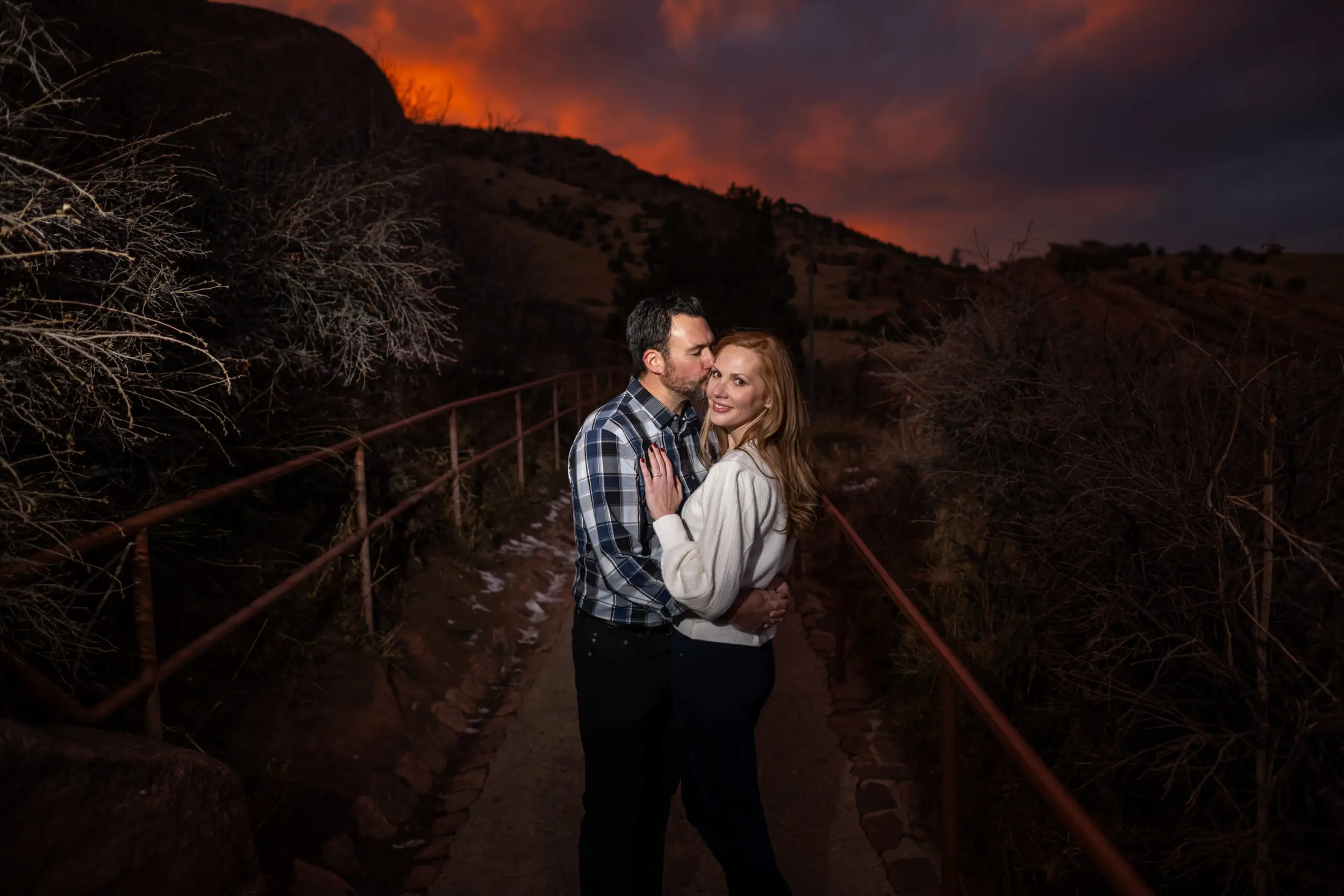 A man kisses a woman as the suns sets at Red Rocks Park and Amphitheatre during a Red Rocks engagement session in Morrison, Colorado.