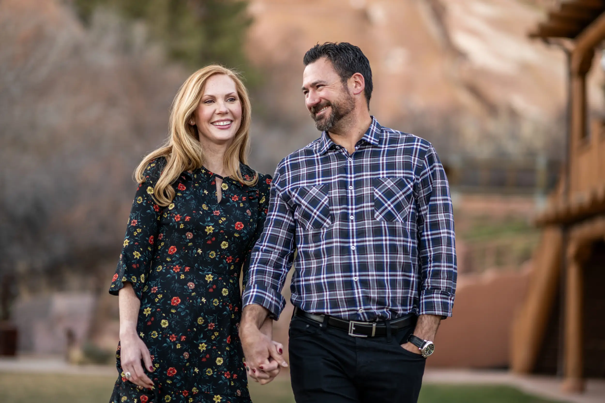 A couple holds hands and laughs while at Red Rocks Park and Amphitheatre during a Red Rocks engagement session in Morrison, Colorado.