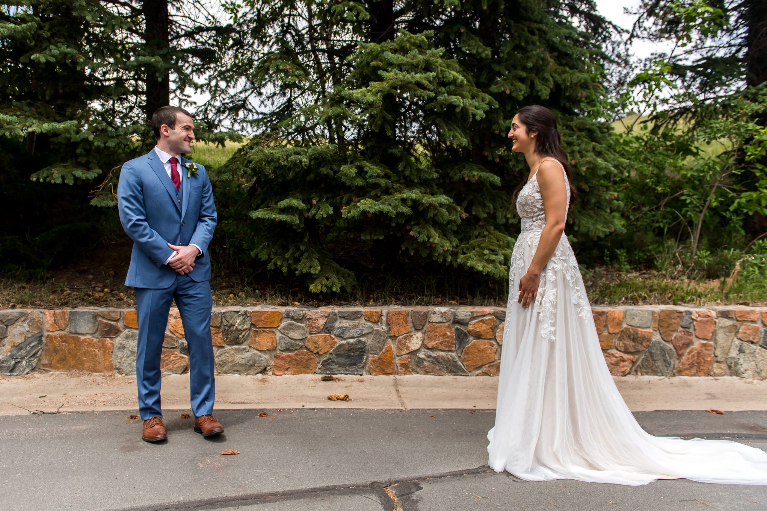 A groom wearing a blue suit turns around to see his bride wearing a long, white wedding dress with a train behind her during a First Look.